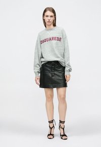Sweat-shirt gris avec l'inscription "DSQUARED2" en lettres bordeaux, associé à une jupe en cuir noire avec des boutons sur le devant et des sandales noires à lanières.