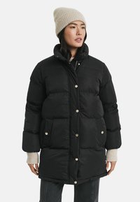 Schwarze Steppjacke mit großen, gesteppten Abschnitten, silbernen Druckknöpfen und seitlichen Taschen. Sie hat einen hohen Kragen und einen dicken Stoff für Wärme.