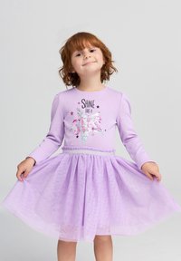 Vestito lilla con maniche lunghe, caratterizzato da una grafica a stella con paillettes e testo. Sovrapposizione di gonna in tulle con un motivo testurizzato. Vita elastica.