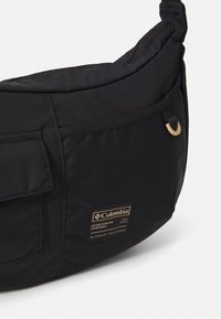 Black Columbia sportswear waist bag with zipper, front pocket, and branded patch showing logo and coordinates.