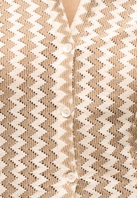 Μπεζ και λευκό ζικ-ζακ πλεκτό ύφασμα με τρία μαργαριταρένια κουμπιά κατά μήκος του κέντρου μιας ζακέτας ή ενός πουλόβερ.