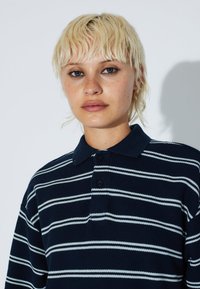 Navy striped polo shirt with white horizontal stripes, made of textured fabric, featuring a buttoned collar and short sleeves.