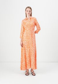 Pitkä, oranssi mekko, jossa on valkoinen aaltohenkilö, kaulus ja pitkähihaiset hihat. Yhdistetty mustiin hihnakenkiin, joka ulottuu lattiaan.