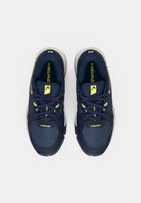 Jūras zila sporta apavi ar acu auduma augšdaļu, teksturētām akcentiem un dzeltenu zīmolu. Iekļauj šņorējamu dizainu un mīkstu zolītes komfortam.