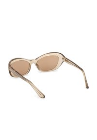 Lunettes de soleil ovales transparentes beige avec des verres teintés marron posées sur une surface blanche.