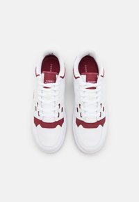 Sneakers bianchi con accenti rossi, pelle testurizzata e pannelli in mesh, caratterizzati da lacci bianchi e logo sulla linguetta. Design atletico classico.