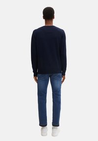 Maglione blu navy a maglia con collo rotondo, abbinato a jeans blu denim e sneakers bianche. Il maglione presenta un delicato dettaglio sul retro.