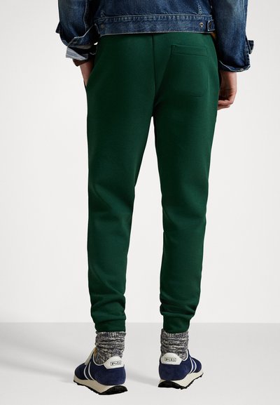 Mørkegrønne joggebukser med slim fit, med en baklomme. Kombinert med blå sneakers og grå mønstrede sokker.