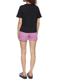 Black cotton T-shirt with short sleeves, paired with light pink denim shorts. Footwear is blue slip-on shoes with a thick black sole.