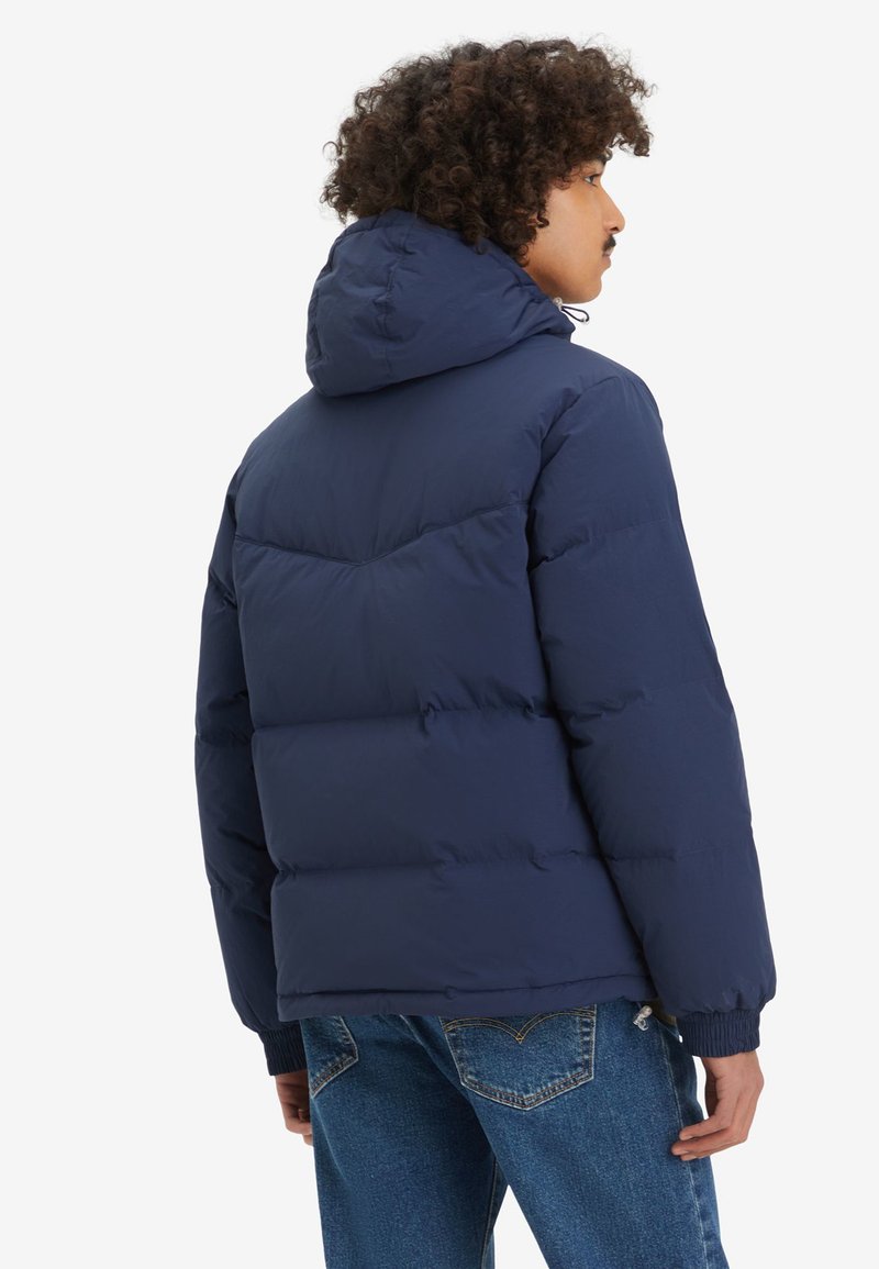Chaqueta acolchada de color azul marino con capucha, diseño acolchado y puños acanalados. Textura suave y lisa con destacadas características de aislamiento.