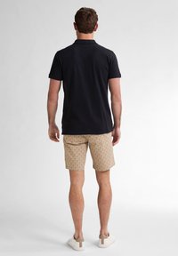 Polo nero, pantaloni corti beige con texture e sneakers bianche. L'outfit presenta una vestibilità classica e un design semplice con accenti minimi.