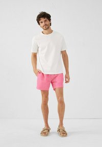 T-shirt bianca in cotone, pantaloni corti rosa e sandali beige. Outfit casual con una vestibilità rilassata e design minimalista.