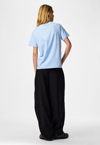 Light blue short-sleeve t-shirt with a relaxed fit, paired with loose black pants. Fabric appears soft; t-shirt has a simple design.