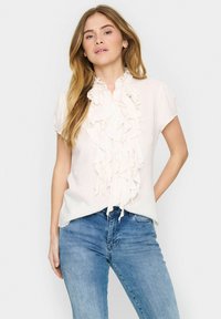 Witte blouse met ruches rond de hals, korte mouwen en een relaxte pasvorm. G gedragen met blauwe denim jeans. Zachte stof en subtiele textuur.
