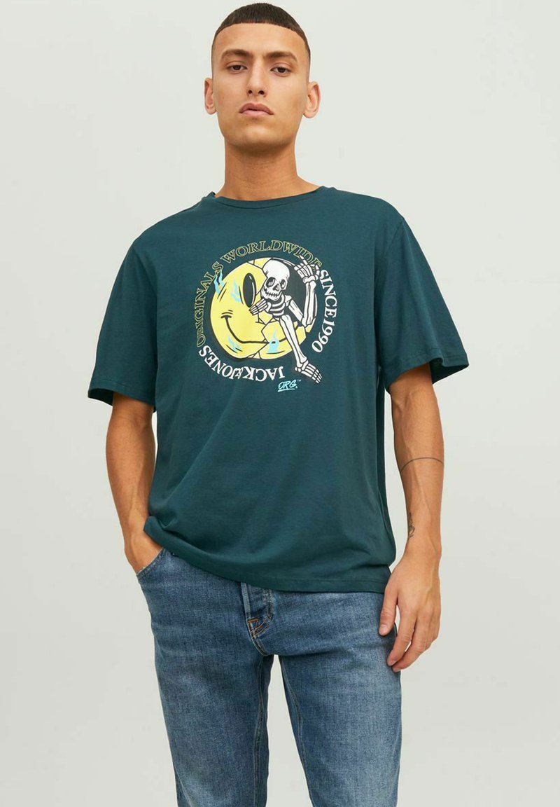Camiseta de algodón verde con cuello redondo, mangas cortas, que presenta un diseño gráfico de un esqueleto y una cara sonriente, corte relajado.