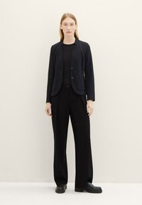 Blazer noir avec un design ajusté et deux boutons, associé à un pantalon noir à jambe large. Le tissu semble lisse avec un léger éclat.