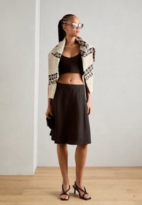 Sort cropped top, svajende mørk nederdel, cremegarn cardigan med mønstre, katteøje solbriller, sort clutch og stiletter på trægulv.