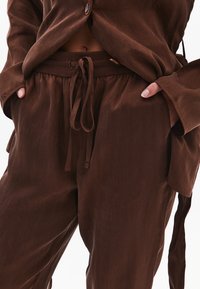 Hnědý lehký loungewear set se zapínáním na knoflíky, dlouhým rukávem a kalhotami s tkaničkou a bočními kapsami. Texturovaný povrch.