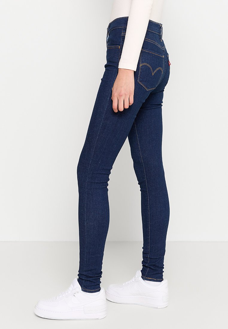 Schmale Jeans aus dunkelblauem Denim mit hoher Taille, Fünf-Taschen-Design und auffälligen herzförmigen Nähten auf den Hintertaschen.