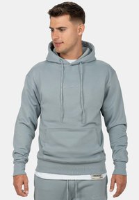 Felpa con cappuccio grigia chiara, dotata di tasca frontale, cordini regolabili, polsini a costine e un ricamo del logo discreto sul petto e sull'orlo.
