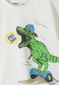 Zielony T-Rex w niebieskiej czapce i żółtych okularach przeciwsłonecznych jedzie na niebieskim hoverboardzie, mówiąc „Chill Dude!” na białym tle materiału.