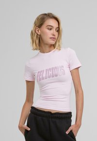 Rozā kokvilnas t-kreklis ar īsām piedurknēm, pieguļošs dizains, uz krūtīm ar punktainiem burtiem uzraksts "FELICIOUS".
