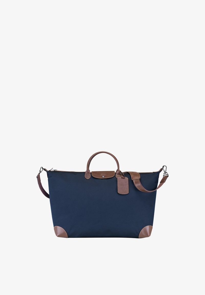 Marineblaue Stofftasche mit braunen Lederakzenten, einem oberen Griff, abnehmbarem Schultergurt und einem angehängten Gepäckanhänger.