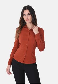 Camicia in cotone color ruggine, con maniche lunghe, taglio aderente e texture liscia. Presenta un colletto a punta e un design con patta frontale.