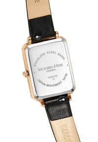 Parte trasera rectangular del reloj con marco de oro rosa, correa de cuero negra y beige, grabada con "Victoria Hyde London" y detalles técnicos.