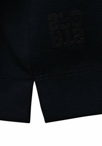 Close-up van zwarte stof met een gestikte zoom en een zwart reliëflogo met het woord "Marc Cain" en gestileerde letters.