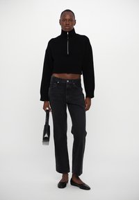 Black cropped sweater with high collar and silver zipper, paired with black straight-leg jeans. Black flats and a clutch bag complete the look.