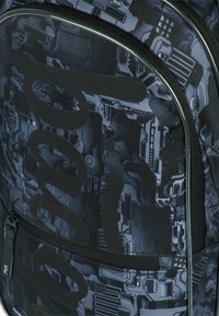 Zaino nero con un pattern grafico testurizzato e disegni simili a circuiti, grande logo nero e dettagli della cerniera in contrasto.