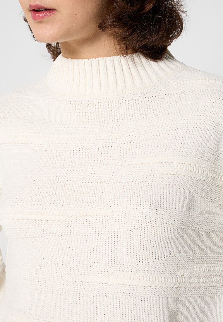 Suéter de punto color beige claro con cuello tipo semi-alto, que presenta rayas verticales texturizadas y un escote acanalado. Tejido suave y texturizado.