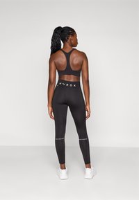 Soutien-gorge de sport noir avec un design dos nageur, associé à un legging noir taille haute. Détails textuels notables en blanc sur le legging.