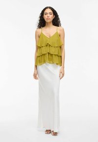 Top de gasa verde oliva en capas con tirantes finos, combinado con una suave falda maxi blanca, creando un contraste en textura y color.