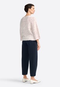 Helles rosa, flauschiges Sweatshirt mit kurzen Ärmeln, kombiniert mit dunkelblauen, schmal zulaufenden Hosen und weißen flachen Schuhen. Einfaches Design, weiche Textur.