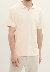 Ljus persikofärgad polo skjorta med korta ärmar, som har ett subtilt palmbladsmönster, mjuk textur och en klassisk kragsdesign.
