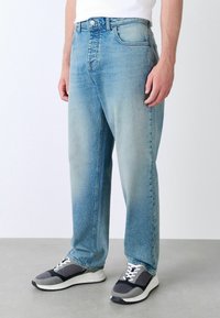 Heledad sinine teksapüksid lõdva lõikega, viie taskuga disain ja kerge fading. Kombineeritud mustade ja hallide spordijalatsitega.