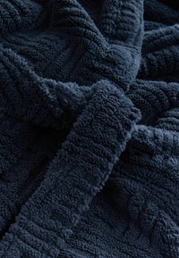 Granatowy pluszowy koc o miękkiej, fakturowanej powierzchni, z paskowym wzorem, który dodaje głębi tkaninie.