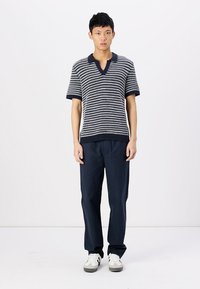 Polo en tricot à rayures marine et crème à manches courtes avec un col en V, associé à un pantalon marine foncé et des baskets blanches. Texture lisse.