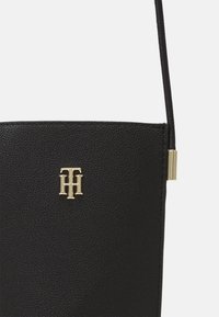 Czarna torebka na ramię z teksturowanej skóry z złotym logo "TH" i cienkim paskiem z metalowym złotym akcentem.