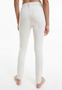 Vaqueros de mezclilla blanca con un diseño ajustado, cintura de altura media y bolsillos traseros. La tela tiene una textura suave y detalles de costura mínimos.