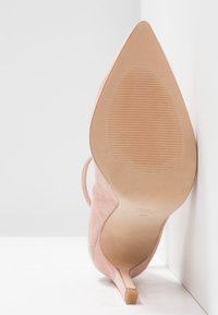 Chaussure à talon haut en suédine rose, avec un bout pointu et un talon aiguille fin. La semelle est lisse avec des rainures pour une meilleure adhérence.