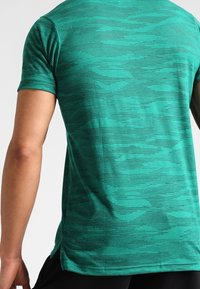 Zelené krátké tričko s krátkým rukávem z texturovaného materiálu s jemným proužkovaným vzorem. Design nabízí pohodlný střih s kulatým lemem.