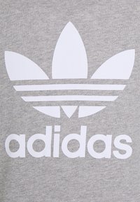 Grå sweatshirt med en stor vit Adidas-logga, som består av tre bladformer och horisontella ränder ovanför varumärkesnamnet.