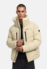 Puhasta jakna u svijetloj bež boji s mekim ovratnikom od krzna. Ima crne patentne zatvarače i oznaku s natpisom "STONE HARBOUR" na rukavu.