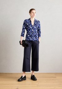 Μπλε πουκάμισο με κουμπιά και λευκό και ανοιχτό μπλε αφηρημένο σχέδιο, ¾ μανίκια, συνδυασμένο με φαρδιά μαύρα παντελόνια και χοντρά μαύρα λουστρίνια.