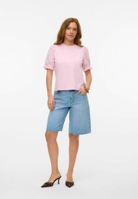 Světle růžové tričko s vyšívanými puff rukávy, kombinované s džínovými šortkami do kolen a hnědými botami na podpatku. Jednoduchý, casual outfit.
