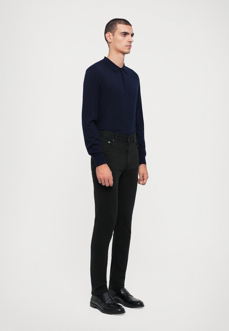 Maritieme langslavige polo met een kraag, gecombineerd met zwarte slim-fit jeans en zwarte instappers. Gladde stof en een getailleerde pasvorm.