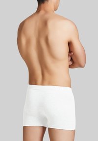 Boxer shorts bianchi in cotone con una texture morbida e un elastico in vita, visti da dietro su uno sfondo grigio neutro.